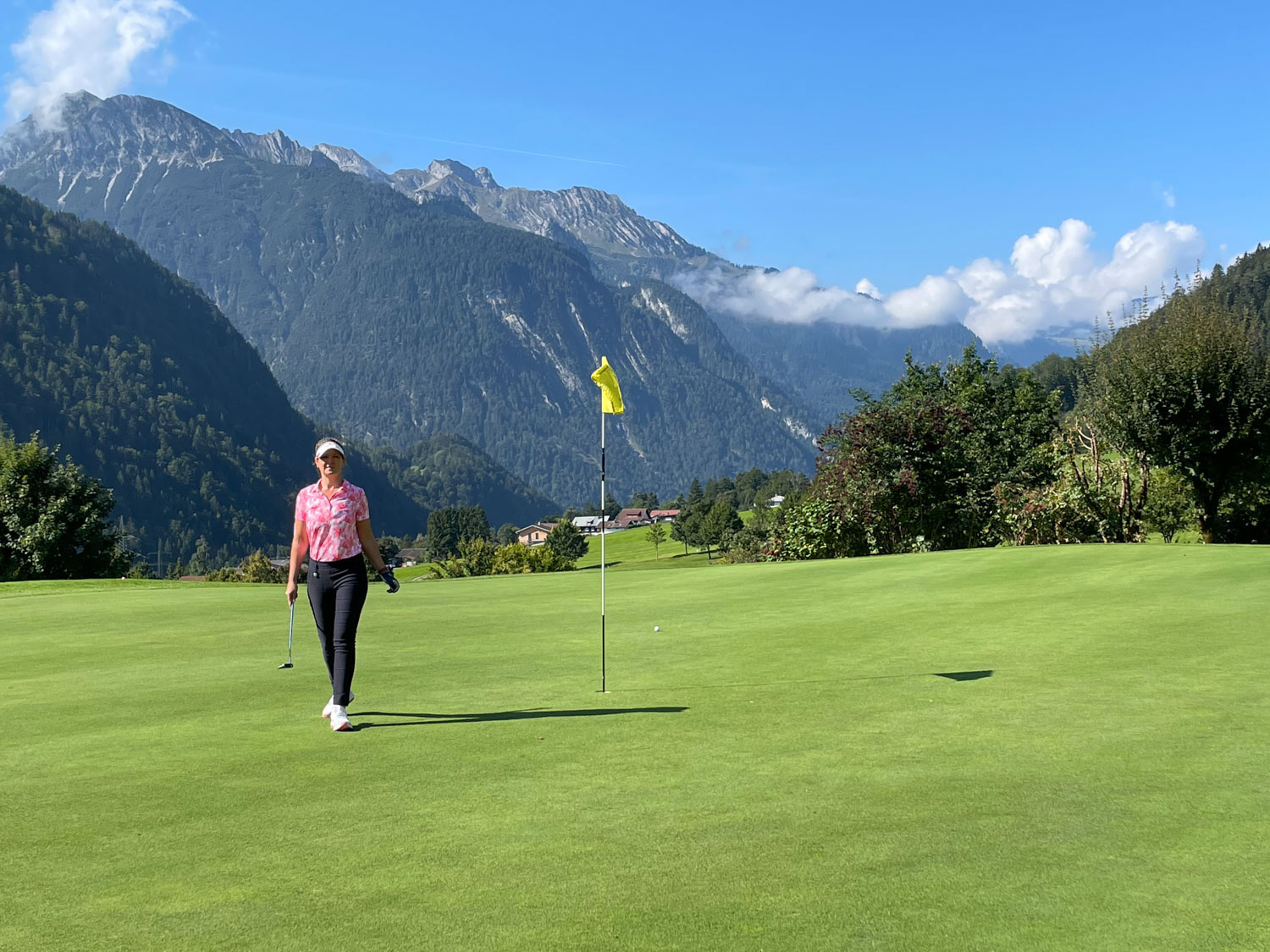 Golfer in rosa Shirt auf dem Grün, dahinter Berge, die so nah sind, dass man sie anfassen könnte – und trotzdem spielt man nur Golf.