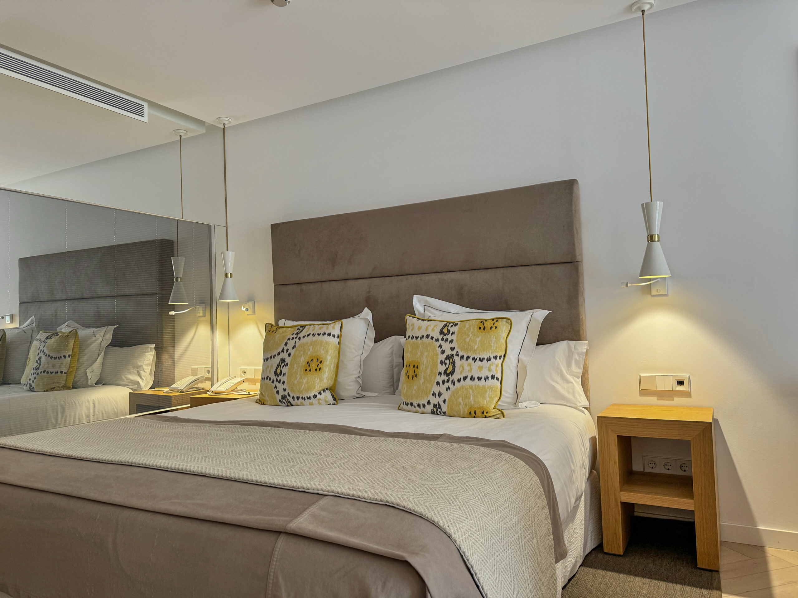 Schlafzimmer mit Taupe-Polsterheadboard, Musterkissen in Gelb und Dunkelblau – wer braucht schon Ablenkung, wenn das Bett selbst schon eine Statement-Aussage ist.