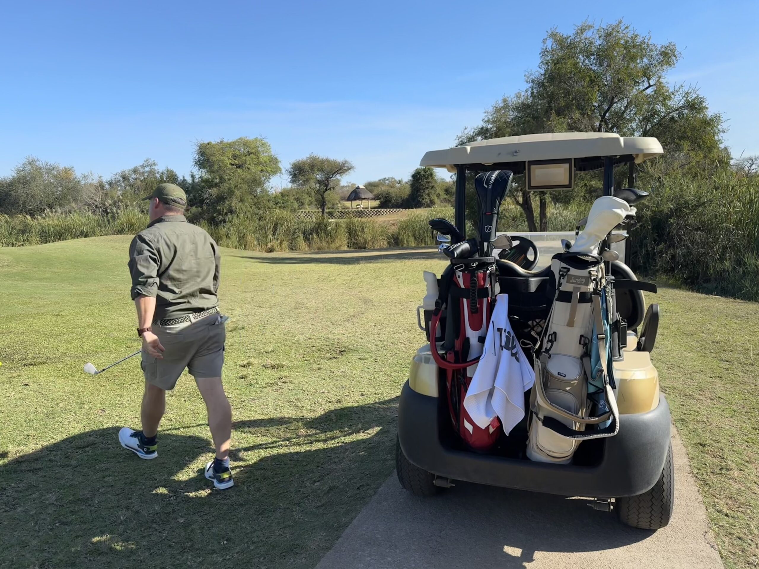 Golfer schlägt Ball, Golfwagen im Hintergrund