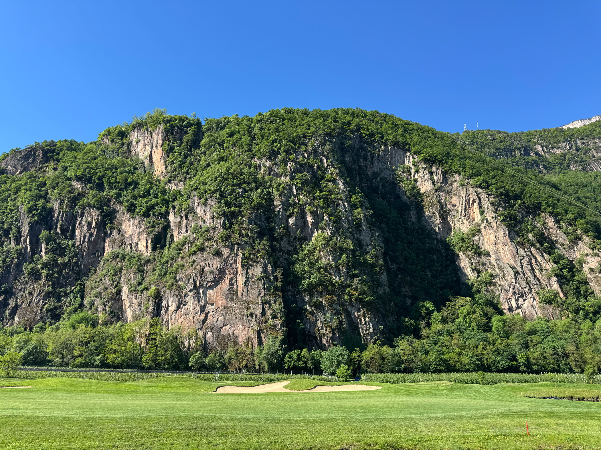 Grüner Golfplatz vor steiler Felswand.