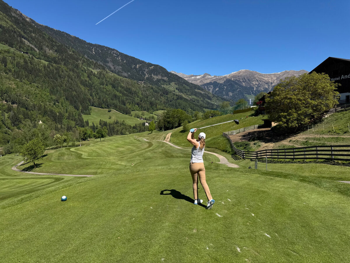Golfspielerin am Abschlag mit Bergpanorama