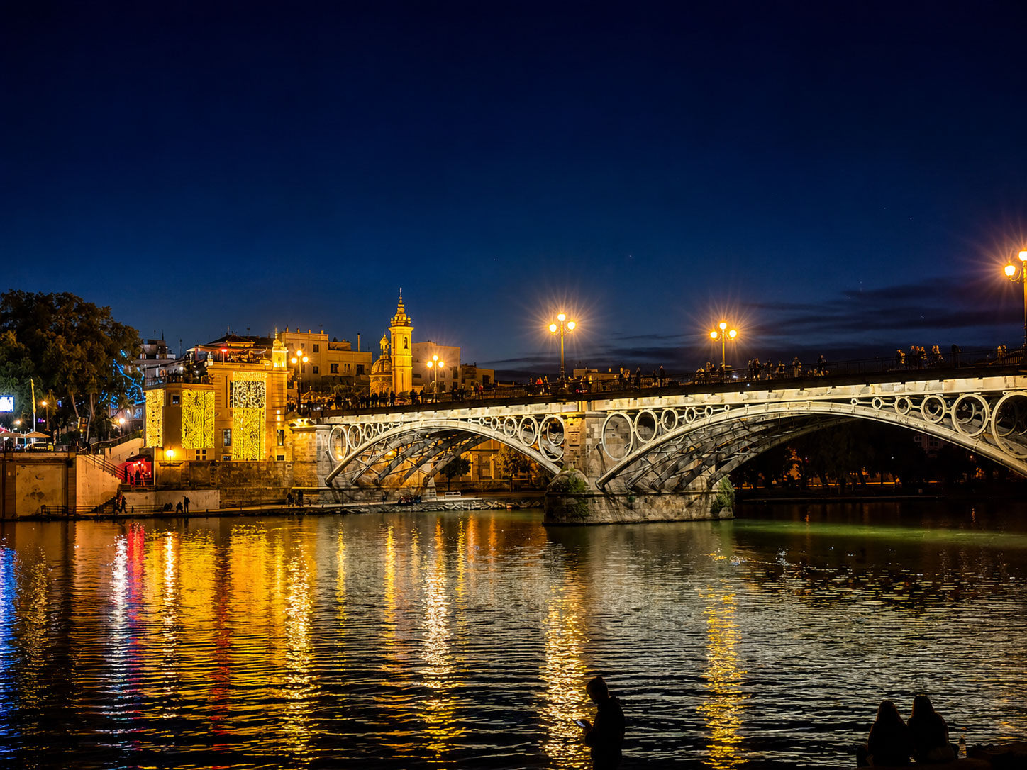 Triana-Brücke über den Guadalquivir in Sevilla bei Nacht mit beleuchteter Skyline