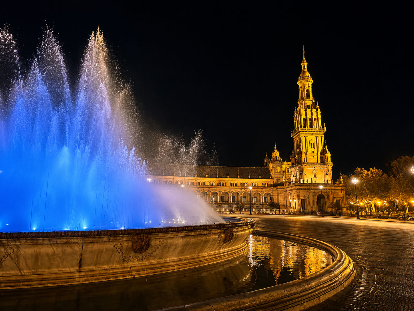 Beleuchteter Springbrunnen vor der Giralda und der Kathedrale von Sevilla am Abend