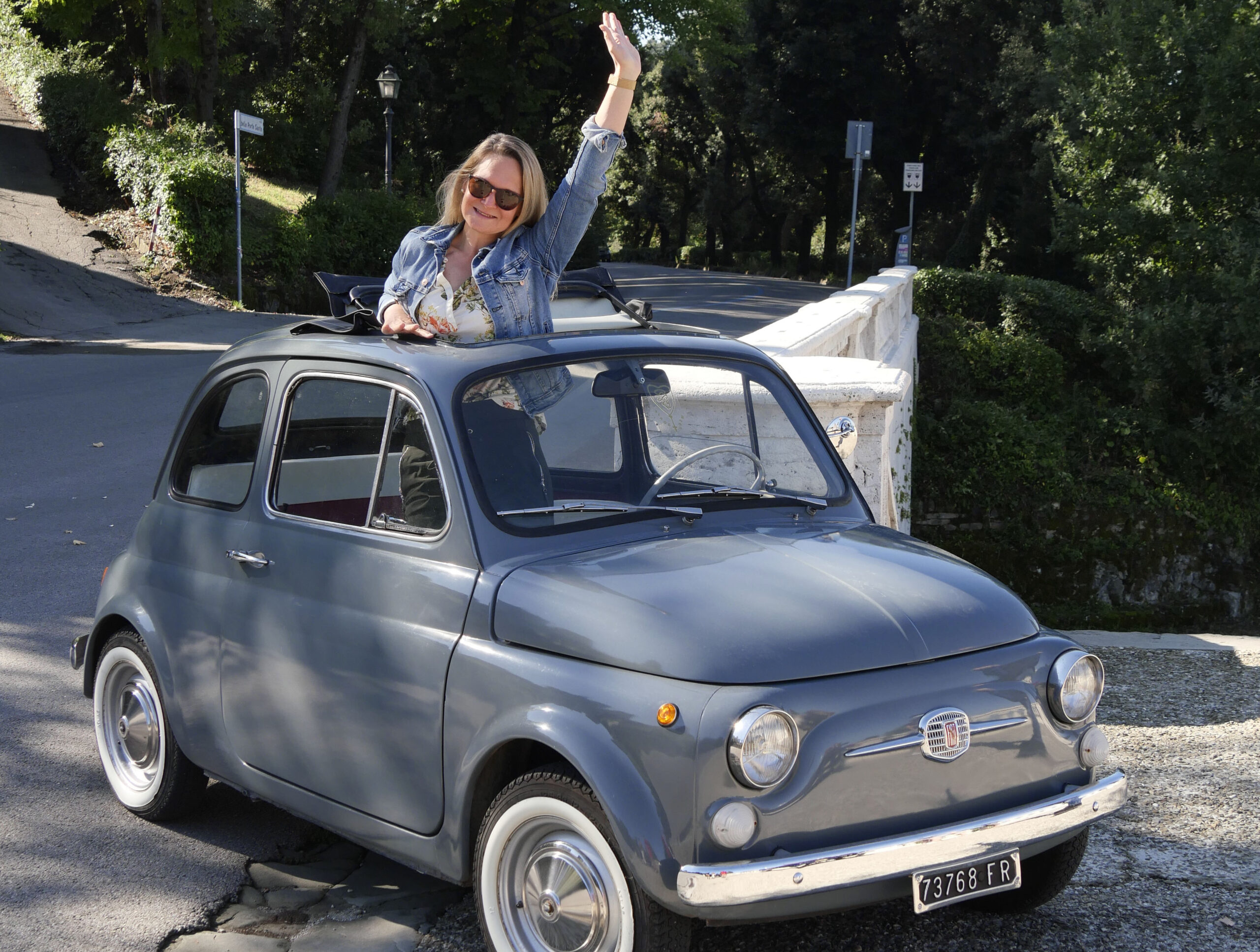 Frau mit Sonnenbrille lehnt aus dem Fiat 500 und winkt – so sieht Sightseeing in Florenz aus, wenn man nicht läuft.